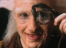 Elderly man in costume peering through a magnifying lens