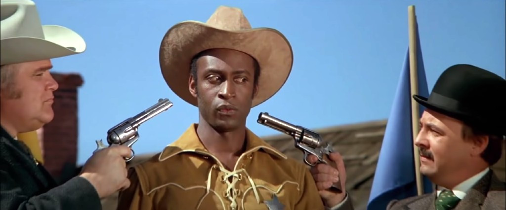 Three cowboys in a western film scene, one holding a revolver